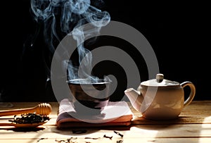 A cup of hot tea with tea pot , hot smoke, dark background.