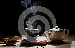 A cup of hot tea with tea pot , hot smoke, dark background.