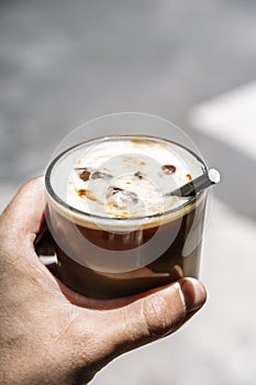 Cup of iced latte cappuccino coffee in hand on city street. Takeaway coffee drink