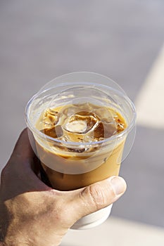 Cup of iced latte cappuccino coffee in hand on city street. Takeaway coffee drink