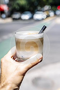 Cup of iced latte cappuccino coffee in hand on city street. Takeaway coffee drink