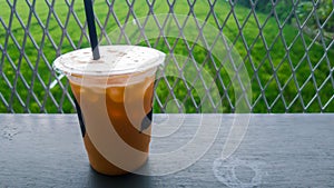 A cup of iced thai tea on wooden table with greeny background