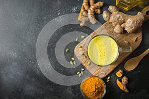 Cup of Indian golden turmeric milk with curcuma powder and ingredients on black. View from above