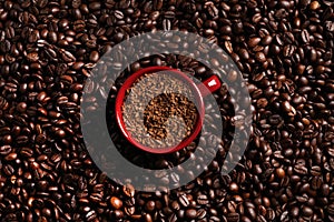 Cup with instant coffee on roasted beans, top view