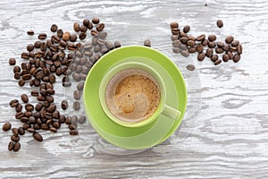 A cup of invigorating coffee and coffee beans on white wooden background. Top down view
