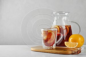 Cup and jug of refreshing iced tea on white table against light background