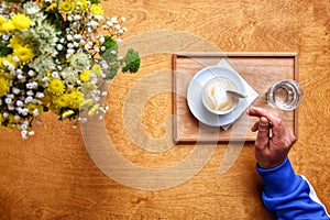 A cup of latte coffee hand with spoon of fresh flowers photo