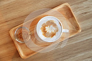 Cup of latte coffee with latte art and brown sugar on wooden tray