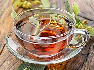 Cup of linden tea and lime flowers on the wooden table.