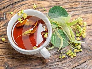 Cup of linden tea and lime flowers on the wooden table. Top view