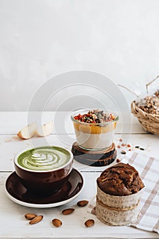 The cup of matcha tea with almond milk , mango pudding and banana muffin at the white table