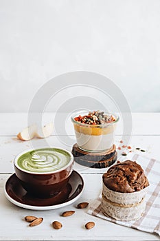 The cup of matcha tea with almond milk , mango pudding and banana muffin at the white table