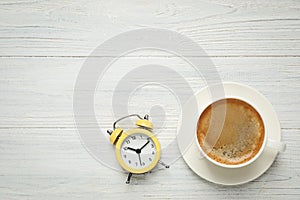 Cup of morning coffee and alarm clock on wooden table, flat lay. Space for text