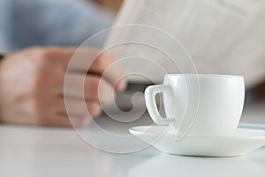 Cup of morning coffee on worktable with businessman reading news