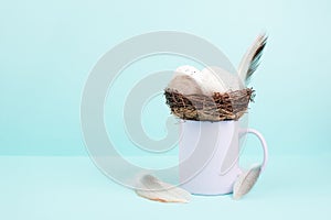 Cup or mug with an easter egg nest and bird feathers, spring holiday greeting card