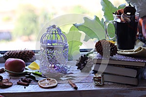 Cup with mulled wine, autumn leaves, seasonal fruits and vegetables, decor, spices on a window background