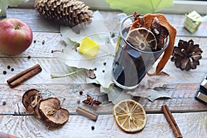 Cup with mulled wine, autumn leaves, seasonal fruits and vegetables, decor, spices on a window background