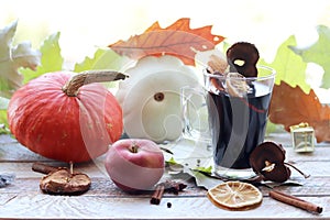 Cup with mulled wine, autumn leaves, seasonal fruits and vegetables, decor, spices on a window background