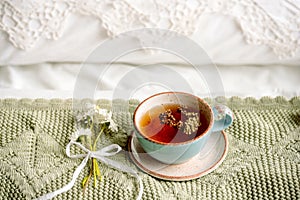 Cup of natural herbal tea from mint and lemon balm in bed,morning close up. Cozy atmosphere.Openwork lace,cotton white blanket,