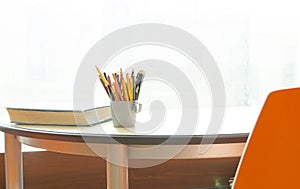 A cup with pencils and a corner of the book on the table by the window. Blurred background. Workplace for study. lightful room