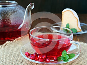 Cup of pomegranate tea with mint and tea pot with a piece of cake
