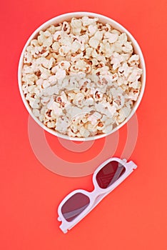 cup with popcorn and 3D glasses on red background, top view. Flat lay. Copyspace