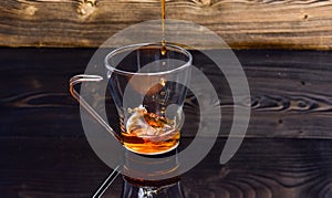 Cup pouring with water or tea with splashes on dark wooden background. Brewing tea concept. Glass with tea pouring with