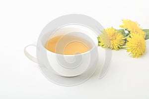 Cup of purifying, diuretic tea of dandelion with fresh leaves and flowers on a white background. Fresh spring organic herbal,