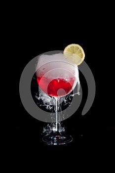 A cup of red cold cocktail with dry ice smoke and a lemon slice