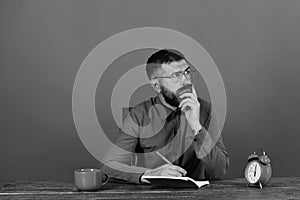 Cup, retro clock and red book on vintage table. Man with thinking face sits at wooden table