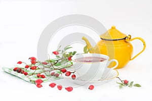 Cup of rose hip herbal tea with rose-hip fruits and pot on white background