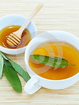 A cup of sage tea with fresh sage and honey.