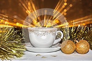 Cup on a saucer. Christmas balls and tinsel. Glowing salute from