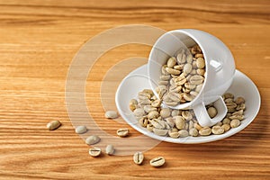 Cup and saucer with green coffee beans on wooden background