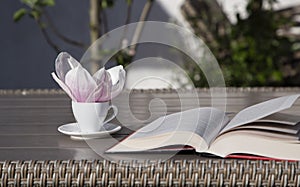 cup with a saucer on the table, there is a large magnolia flower in it, an open book