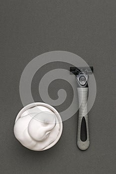 A cup with shaving foam and a grey razor on a grey background