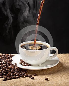 Cup of steamy coffee with smoke and coffee beans. Hot coffee on black background
