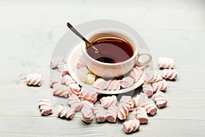 Cup and sweets prepared as dessert. Mug filled with black brewed tea, spoon and heap of marshmallow on white wooden