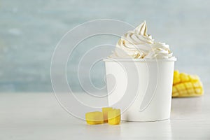 Cup with tasty frozen yogurt and mango on light wooden table
