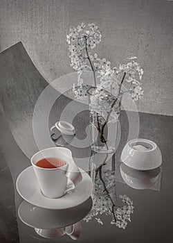 A cup of tea alongside a transparent glass vase holding delicate white flowers