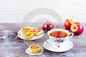 Cup of tea and apple roses shaped muffins on rustic wooden table