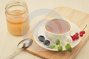 Cup of tea with berries and mint in a saucer and honey/cup of tea with berries and mint in a saucer on a wooden tray and honey.