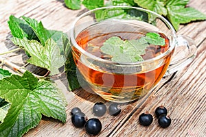 A cup of tea with black currant leaves. Tea with currants on a wooden table