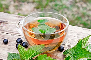 A cup of tea with black currant leaves. Tea with currants on a wooden table in the open air
