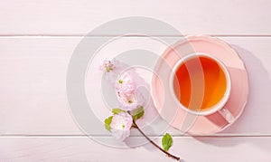 Cup of tea and blossoming Almond Prunus triloba branch on light pink wooden table and copy space for text