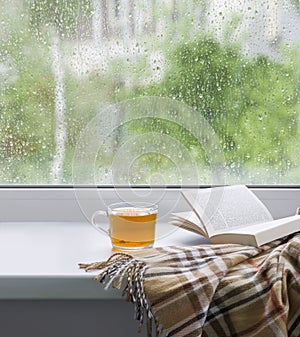 A cup of tea, a book and a plaid on the windowsill on a rainy day