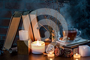 A cup of tea, books, candles, smoke. Mysterious dark still life. Dried flowers. Fairy atmosphere