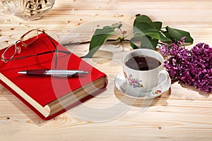 Cup of tea, branch of lilacs, book, spectacles and pen