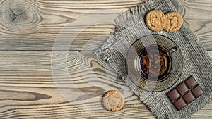 Cup of tea on a burlap napkin with cookies and chocolate on a wooden background. artistic mockup with copy space