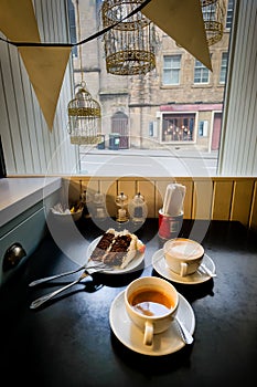 Cup of tea, cappuccino and a red velvet cake on a plate on the window sill of a small cafe.